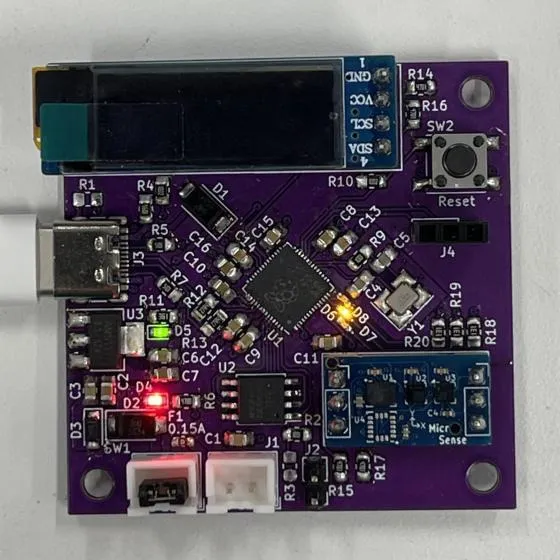 The same board assembled and powered. A narrow OLED display is mounted across the top edge with its pins labelled GND, VCC, SCL and SDA, a USB-C cable is plugged into the left edge, and a small blue sensor breakout is fitted at the lower right. The microcontroller carries the Raspberry Pi logo, a red power LED and a green LED are lit at the left, and an amber LED is lit beside the crystal.